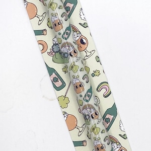 May include: A stylus pen with a clear barrel featuring a repeating pattern of cartoon beer mugs, rainbows, and shamrocks. The pen is on a light green patterned backing with the words "Scribbles and Script".