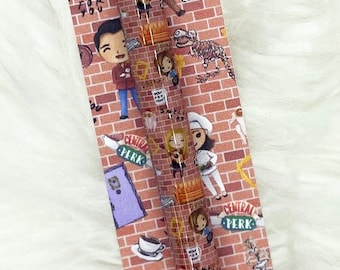 Op de afbeelding: Decoratieve pen met een bakstenen muurontwerp, cartoonfiguren en de tekst "Central Perk". De pen heeft een zwarte inktcartridge en een zilverkleurige metalen punt. De tekst "I'll be there for you" is ook zichtbaar.