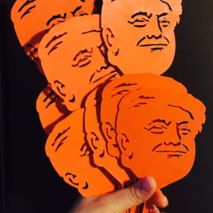 Peut inclure: Un ensemble de six silhouettes en plastique orange d&eacute;coup&eacute;es d'un visage humain. Les d&eacute;coupes sont tenues dans une main.