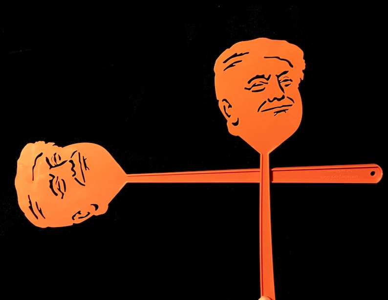 Peut inclure: Deux raquettes &agrave; mouches en plastique orange en forme de visage. Les raquettes sont crois&eacute;es au niveau des manches.