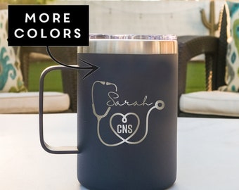 May include: A dark gray travel mug with a stainless steel lid and handle. The mug is engraved with a stethoscope, a heart, and the text "Sarah CNS".