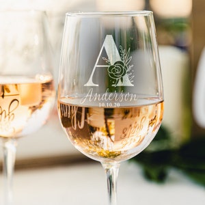 Może przedstawiać: Dwa przezroczyste kieliszki do wina z wygrawerowanym wzorem kwiatowym na boku. Kieliszek po prawej stronie ma literę "A" z kwiatowym wzorem i tekstem "Anderson 10.10.20". Oba kieliszki są wypełnione różowym winem.
