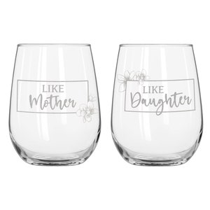May include: Two clear glass wine glasses with the text "Like Mother" and "Like Daughter" etched on them. Each glass has a floral design.