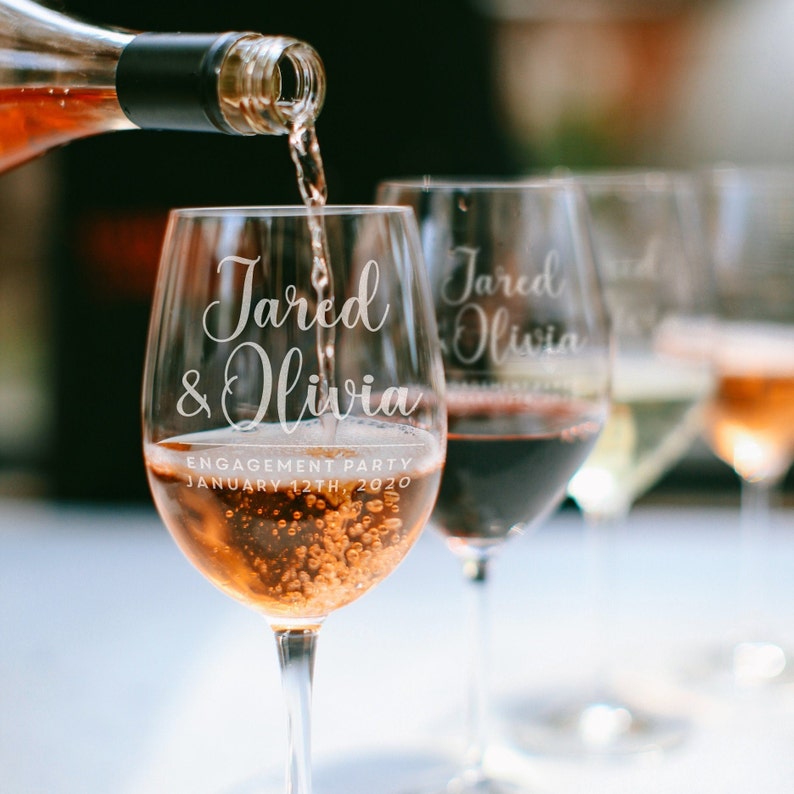 May include: Two clear wine glasses with the names "Jared & Olivia" etched on them. The glasses are filled with rose wine and the text "Engagement Party January 12th, 2020" is also etched on the glass.
