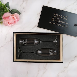 Könnte beinhalten: Eine schwarze Holzkiste mit einem Deckel, auf dem "CHASE & Chelsie - 04.22.17" steht. In der Kiste befinden sich zwei Champagnerflöten mit der gleichen Gravur.