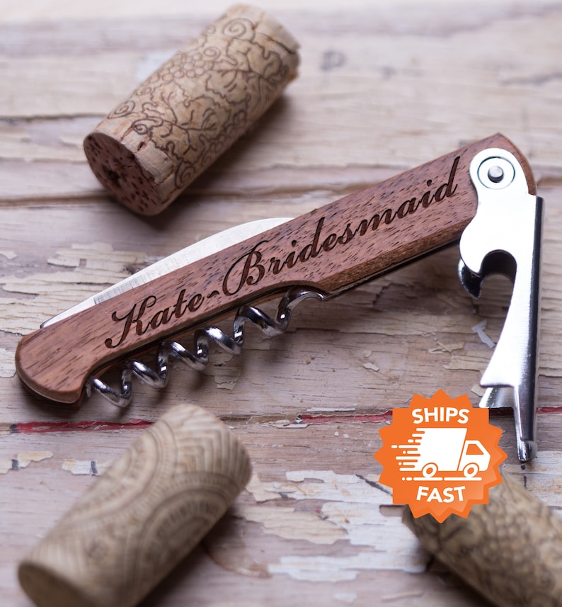 May include: A wooden wine opener with a corkscrew and bottle opener. The handle is engraved with the text "Kate - Bridesmaid".