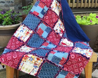 May include: A red, white, and blue patchwork quilt with a cowboy theme. The quilt is made of various fabrics, including bandana print, gingham, and solid colors. The quilt is fringed and has a blue backing.