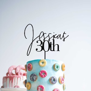 May include: A blue cake decorated with colourful mini doughnuts and topped with a black acrylic cake topper that says "Jessica 30th".