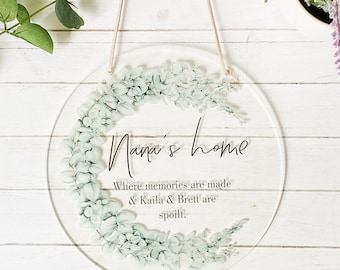 May include: A round, clear acrylic sign with a floral design and the text "Nana's home Where memories are made & Kaila & Brett are spoilt."