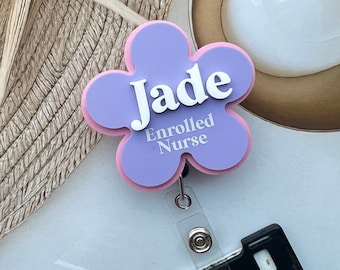 Op de afbeelding: Paarse badgehouder in de vorm van een bloem met een roze rand. De badgehouder heeft de naam "Jade" en de tekst "Enrolled Nurse" in wit.