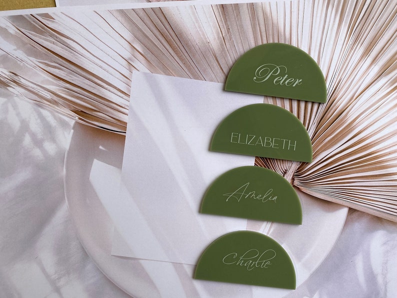 May include: Four green half-circle place cards with white calligraphy names: Peter, Elizabeth, Amelia, and Charlie.