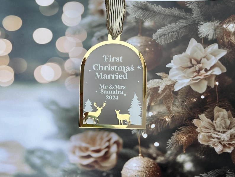 May include: A gold-framed Christmas ornament with the text "First Christmas Married" and the names "Mr & Mrs Samalra 2024". The ornament features deer and tree silhouettes. A gold ribbon is attached for hanging.