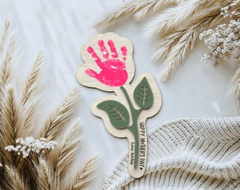 May include: Wooden handprint flower craft with pink handprint and green leaves. The craft says "Happy Mother's Day" and "Love Archie".