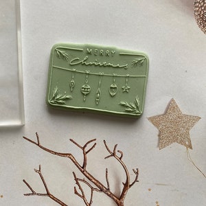 May include: A green rubber stamp with the text "Merry Christmas" and a design of hanging ornaments.