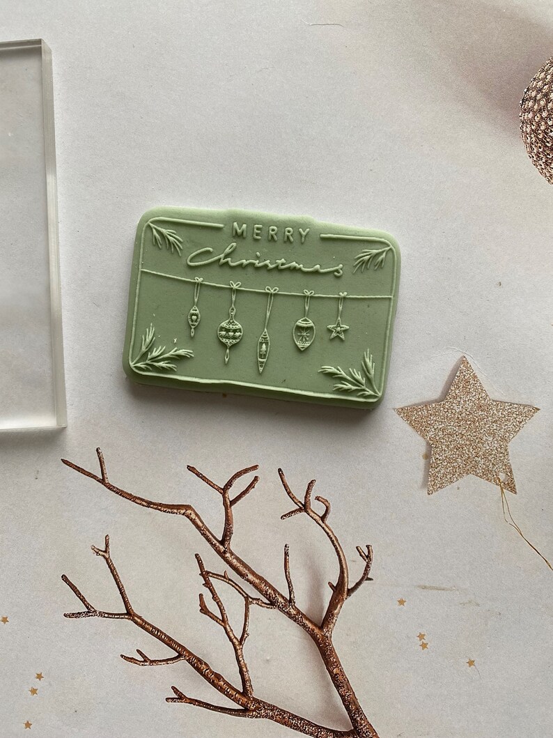May include: A green rubber stamp with the text "Merry Christmas" and a design of hanging ornaments.