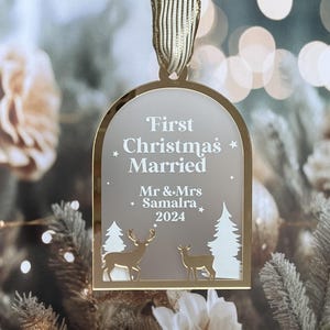 May include: A gold-toned Christmas ornament with a ribbon for hanging. The ornament features the text "First Christmas Married" and the names "Mr & Mrs Samalra 2024". The design includes deer and trees, perfect for a newlywed couple's first holiday season.