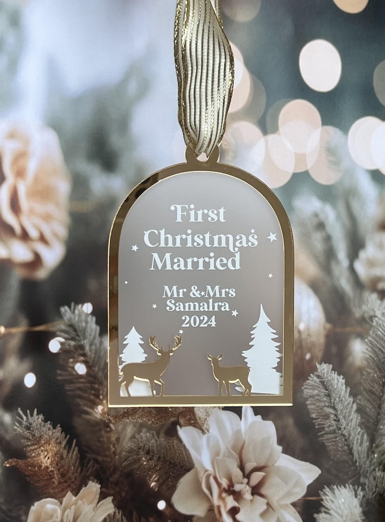 May include: A gold-toned Christmas ornament with a ribbon for hanging. The ornament features the text "First Christmas Married" and the names "Mr & Mrs Samalra 2024". The design includes deer and trees, perfect for a newlywed couple's first holiday season.