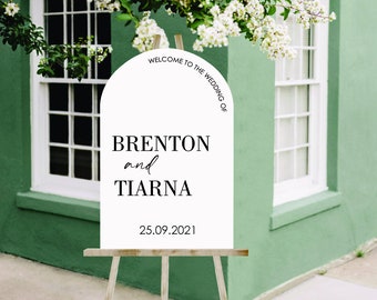 May include: White welcome sign with a rounded arch top. The sign reads "Welcome to the Wedding of Brenton and Tiarna 25.09.2021". The sign is on an easel.