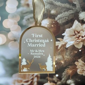 May include: A gold-colored Christmas ornament with the text "First Christmas Married" and the names "Mr & Mrs Samalra 2024". The ornament features deer and tree silhouettes. It hangs from a gold ribbon.