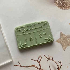 May include: A green rubber stamp with the text "Merry Christmas" and a design of hanging ornaments.