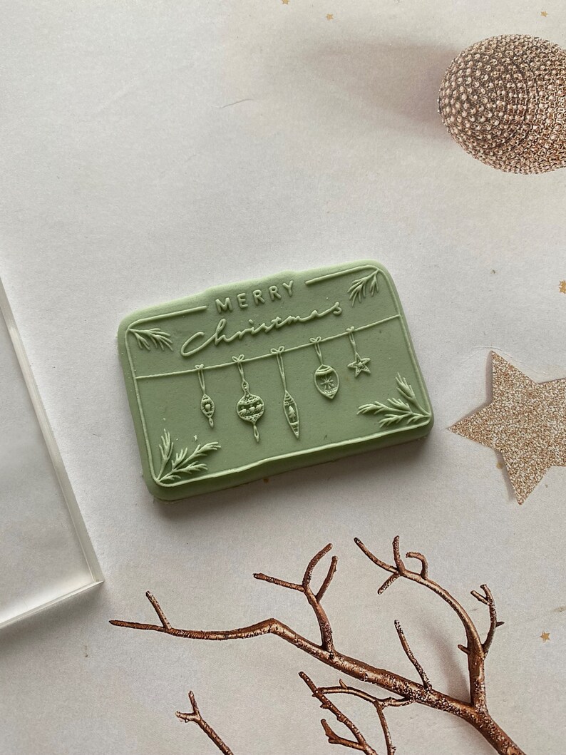 May include: A green rubber stamp with the text "Merry Christmas" and a design of hanging ornaments.