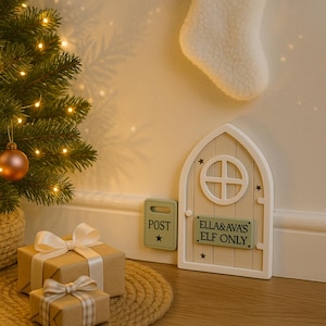May include: A decorative fairy door and mailbox set in cream and pale green, with the text "ELLA&AVA'S ELF ONLY". The door has a circular window. A small Christmas tree with fairy lights and wrapped gifts are also in the image, creating a festive scene.