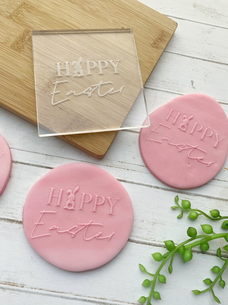 May include: A clear acrylic stamp with the text "HAPPY Easter" and a bunny rabbit graphic. The stamp is used to create impressions on pink clay circles with the same text.