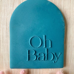 Puede incluir: Sellos de goma en forma de arco de color azul turquesa con las palabras "Oh Baby" en relieve en blanco.