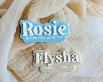 Puede incluir: Dos etiquetas de nombre azules y blancas con texto blanco. La etiqueta superior dice "Rosie Registered Nurse/Midwife". La etiqueta inferior dice "Elysha assistant in nursing".
