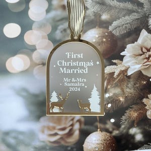 May include: A gold-framed Christmas ornament with the text "First Christmas Married" and the names "Mr & Mrs Samalra 2024". The ornament features deer and trees. A gold ribbon is attached for hanging.