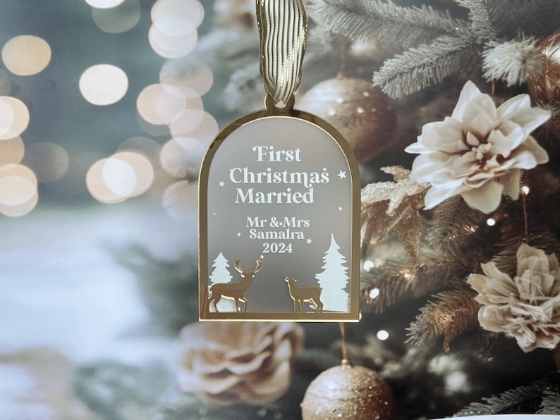 May include: A gold-framed Christmas ornament with the text "First Christmas Married" and the names "Mr & Mrs Samalra 2024". The ornament features deer and trees. A gold ribbon is attached for hanging.