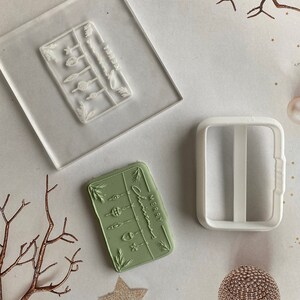 May include: A set of two clear acrylic Christmas stamp blocks. One block features a design of a string of Christmas lights with the text "Merry Christmas". The other block is a blank rectangle with a handle.