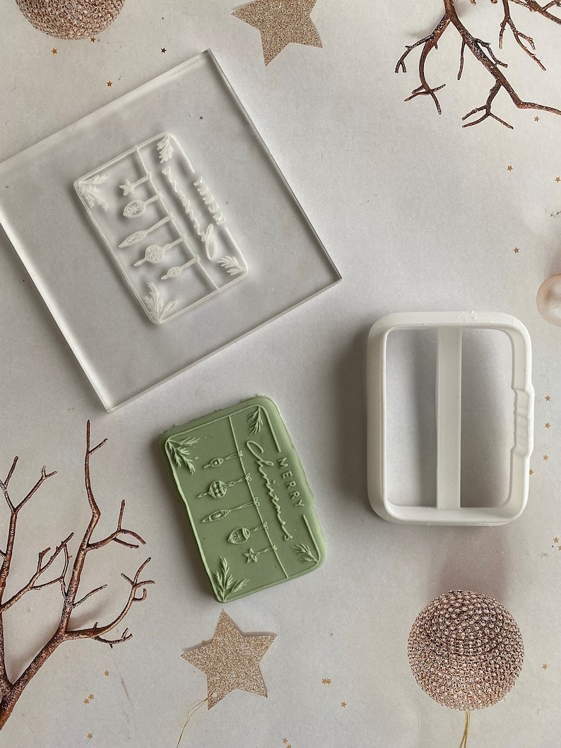 May include: A set of two clear acrylic Christmas stamp blocks. One block features a design of a string of Christmas lights with the text "Merry Christmas". The other block is a blank rectangle with a handle.
