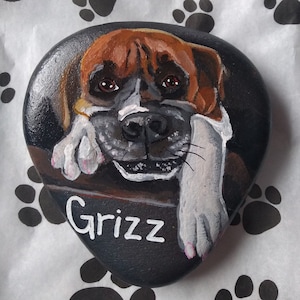 May include: Hand-painted rock art of a brown and white dog with the name "Grizz" written in white paint.