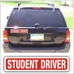 May include: A black SUV with a red and white "STUDENT DRIVER" bumper sticker. The sticker is rectangular with white text on a red background. The vehicle has a license plate and a rear wiper.