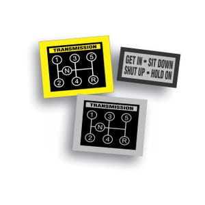May include: Three stickers, two with a black and white illustration of a car's transmission gear shift pattern and the word "TRANSMISSION" above it, and one with the text "GET IN - SIT DOWN SHUT UP - HOLD ON".
