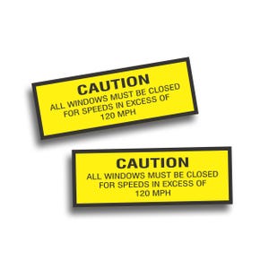 May include: Two rectangular yellow caution stickers with black borders. The text on the stickers reads "CAUTION ALL WINDOWS MUST BE CLOSED FOR SPEEDS IN EXCESS OF 120 MPH."