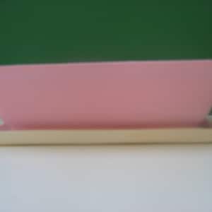 May include: A pink ceramic planter with a white base. The planter is rectangular and has a smooth, glossy finish.