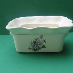 May include: White ceramic planter with a scalloped rim and a floral design featuring purple flowers. The planter has a removable inner pot.