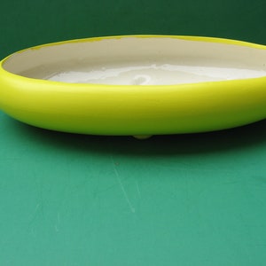 May include: A bright yellow oval ceramic planter with a white interior. The planter is sitting on a green surface.