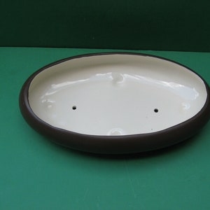 May include: A brown oval ceramic planter with a white interior. The planter has two drainage holes in the bottom.