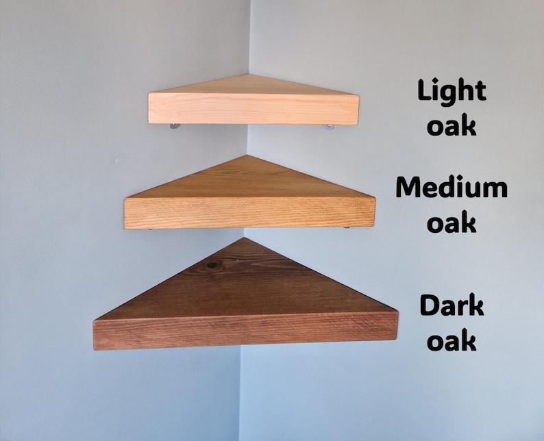Op de afbeelding: Drie houten hoekplanken in lichte, medium en donkere eikentinten zijn aan een lichtblauwe muur bevestigd. De planken zijn driehoekig, met de tekst "Light oak", "Medium oak" en "Dark oak" naast elke plank.