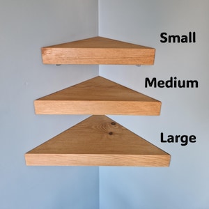 Op de afbeelding: Drie houten hoekplanken in verschillende maten: klein, medium en groot. De planken zijn driehoekig, met een natuurlijke houtnerf afwerking. Ze zijn gemonteerd op een lichtblauwe muur. De tekst "Small", "Medium" en "Large" wordt weergegeven.