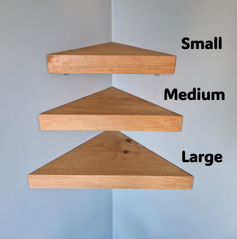 Op de afbeelding: Drie houten hoekplanken in verschillende maten: klein, medium en groot. De planken zijn driehoekig, met een natuurlijke houtnerf afwerking. Ze zijn gemonteerd op een lichtblauwe muur. De tekst "Small", "Medium" en "Large" wordt weergegeven.