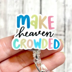 May include: A colorful badge reel with the text "Make heaven crowded" in a white background. The badge reel is made of clear plastic and has a metal clip.