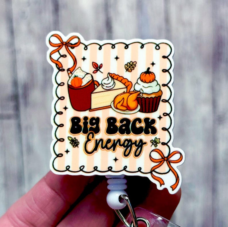 May include: A rectangular badge with a Thanksgiving theme, featuring a striped background and the phrase "Big Back Energy." The badge includes illustrations of a pumpkin spice latte, pie, turkey, and a cupcake.
