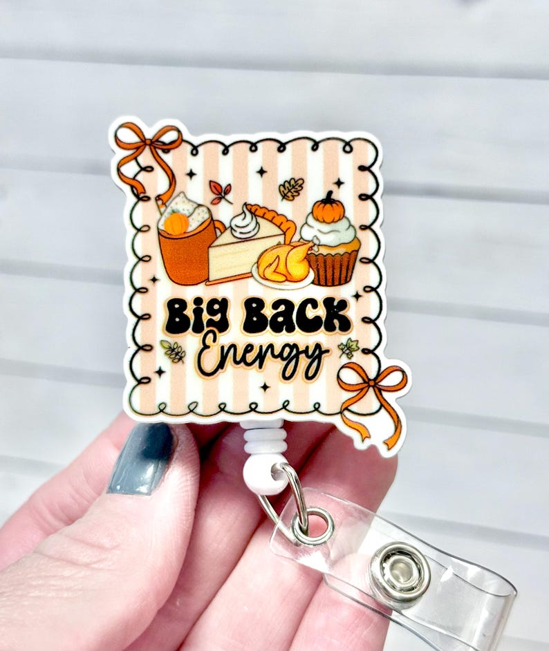 May include: A retractable badge reel with a fall-themed design. The design features a pumpkin spice latte, pie, and a cupcake with the words "Big Back Energy". The reel has a clear plastic strap and a metal snap.