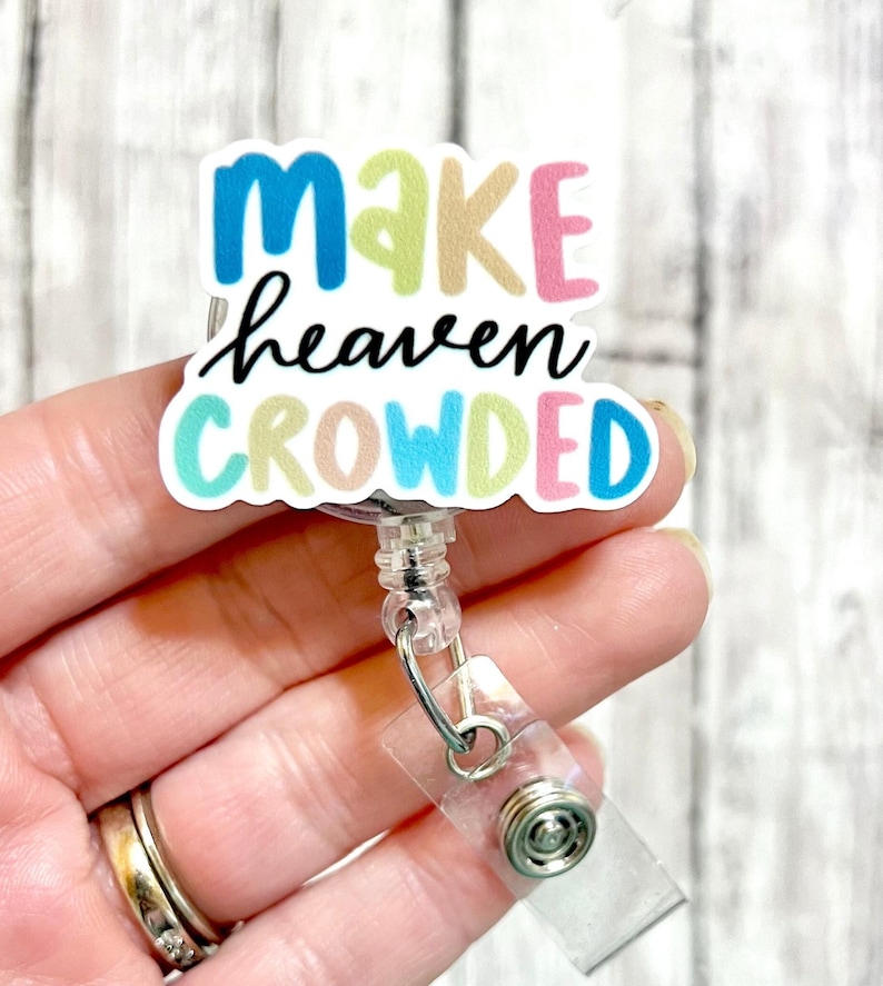 May include: A colorful badge reel with the text "Make heaven crowded" in a white background. The badge reel is made of clear plastic and has a metal clip.