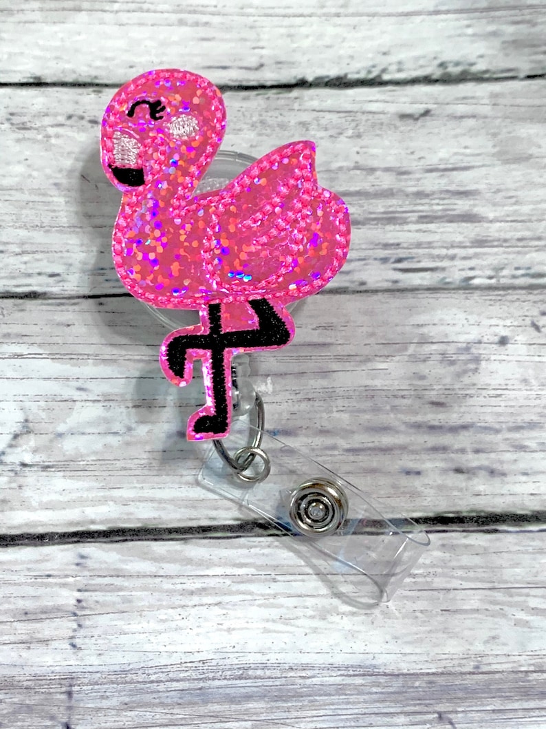 May include: Pink glitter flamingo with black eyes and a black leg, attached to a clear plastic retractable badge holder.