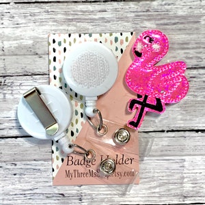 May include: Pink glitter flamingo badge holder with a white retractable badge reel and a clear plastic badge holder. The badge holder has the text "Badge Holder" and "MyThreeMsCraftsy.com".